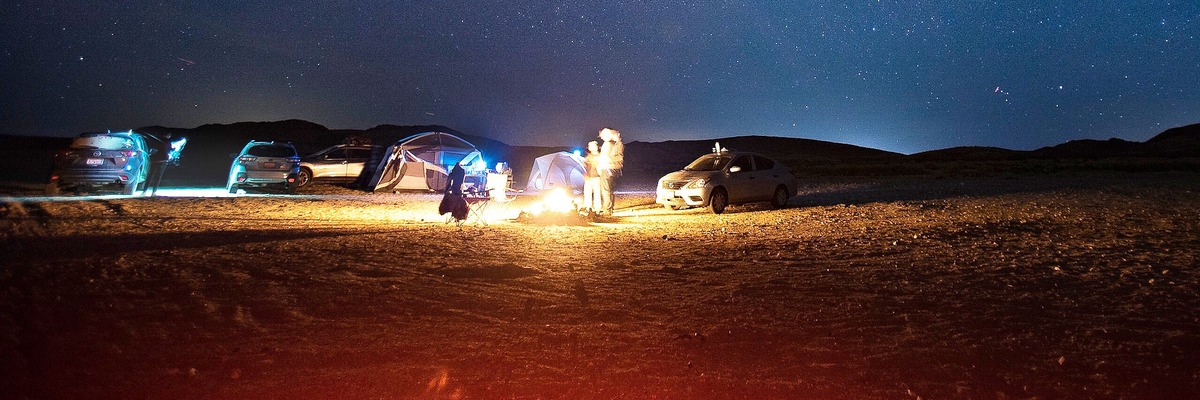 Aufmerksamkeitsbasierter Zuschnitt des Wüstenfotos mit 1200×400, bei dem Autos, Zelte, Lagerfeuer und Menschen vollständig im Bild bleiben.