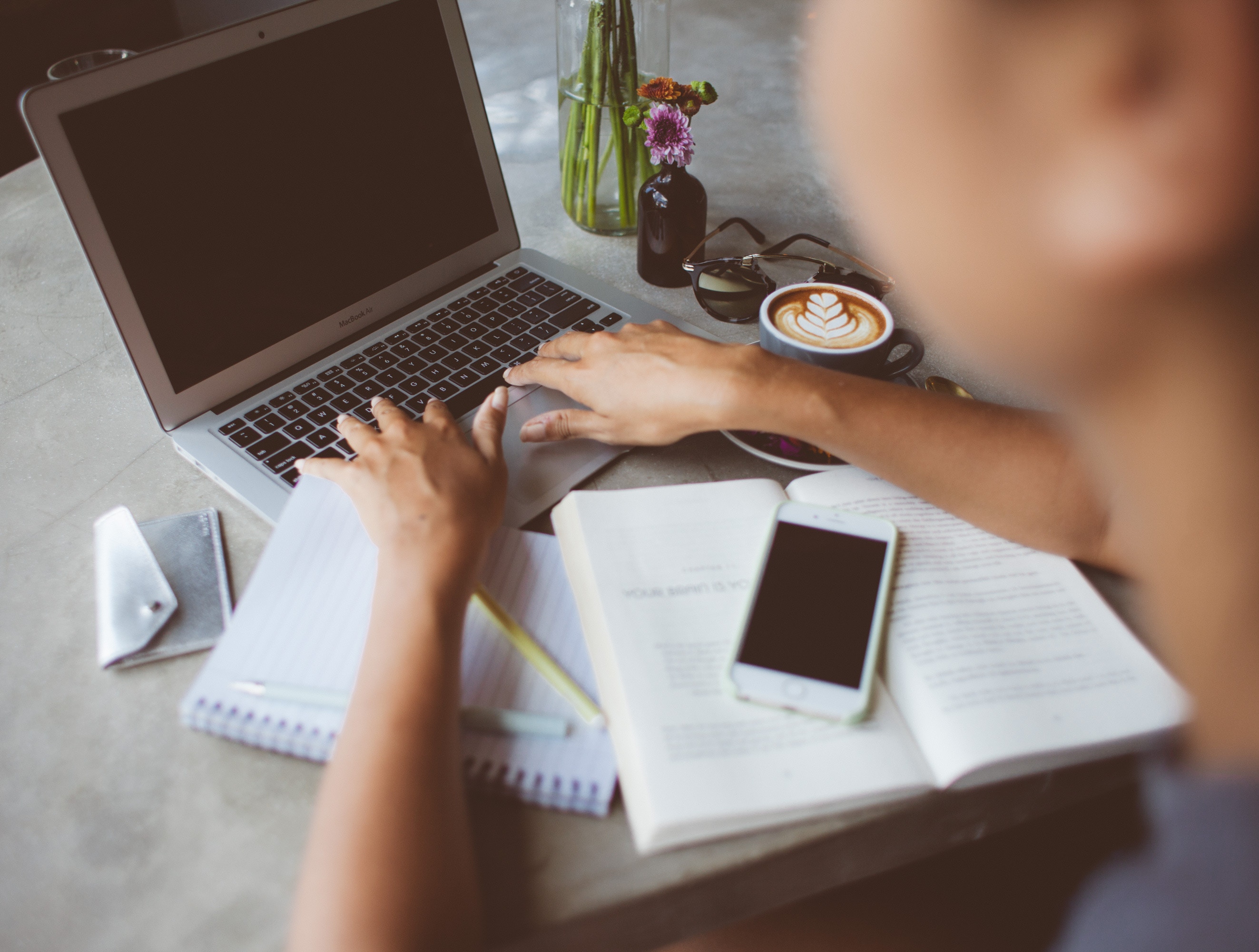 A stock photo of someone typing on a laptop, with a notepad and coffee in front of them.